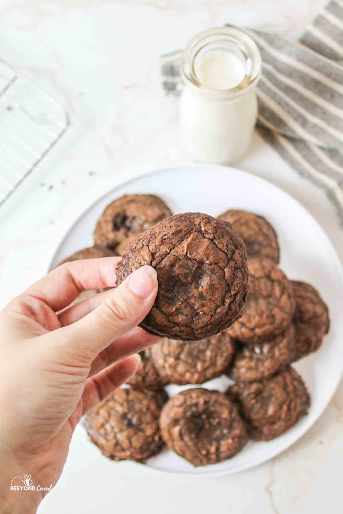 ahand holding up a brownie cookie above a plate with more cookies on it