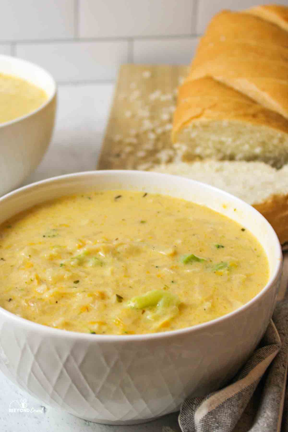 a close up of a bowl filled with cheddar potato soup with bread loaf sliced in background