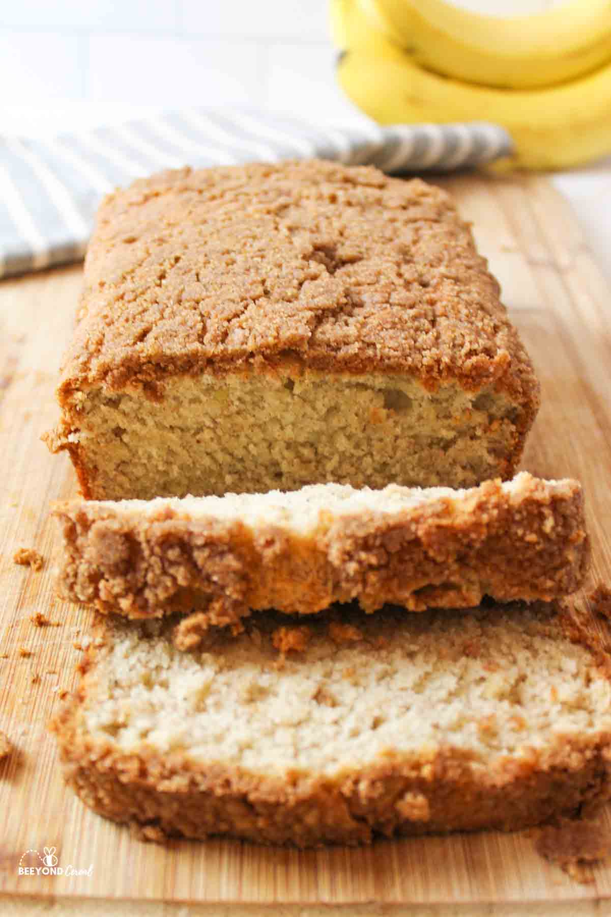 an upclose view of sliced banana bread on a cutting board with yellow bananas in background
