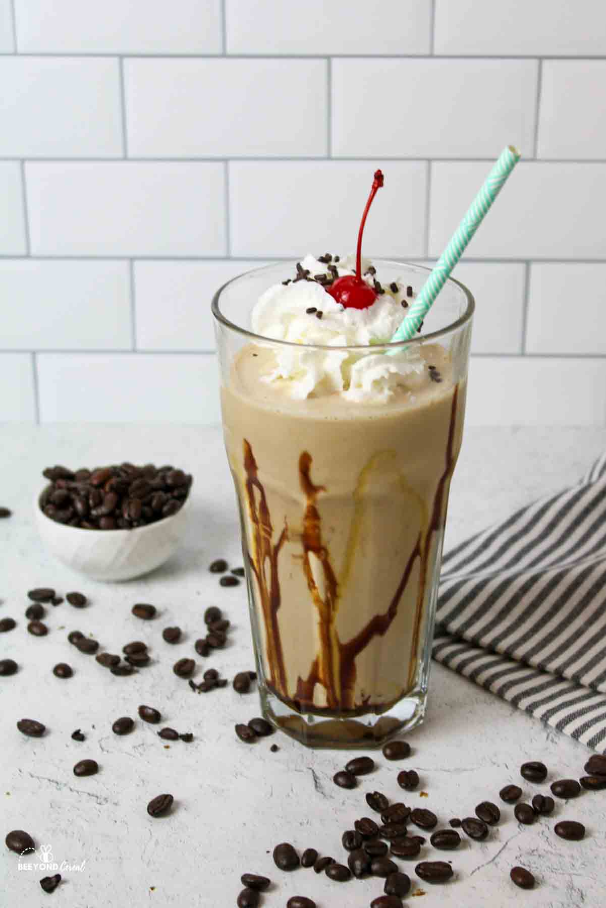 a glass of coffee milkshake with scattered coffee beans around it.