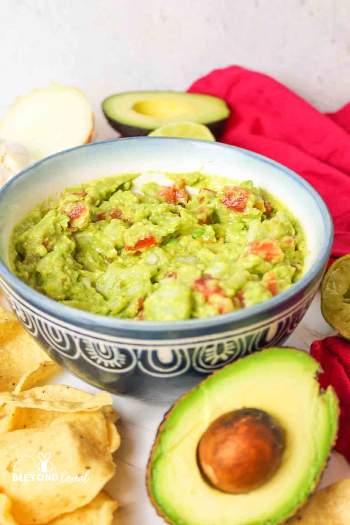 an upclose view of guacamole in a blue bowl next to tortilla chips and half an avocado
