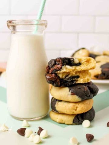 a glass of milk next to a stack of marbled chocolate chip cookies and scattered chocolate chips.