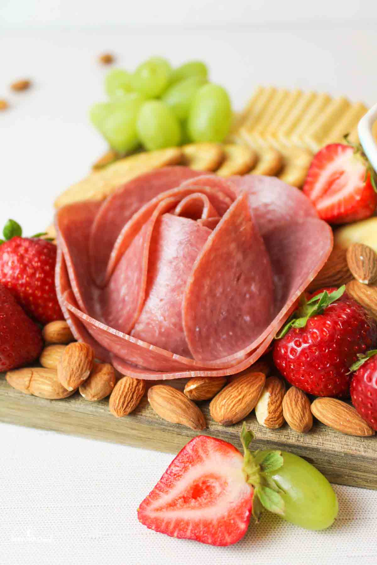 a meat flower on a charcuterie board with strawberries and almonds around it.