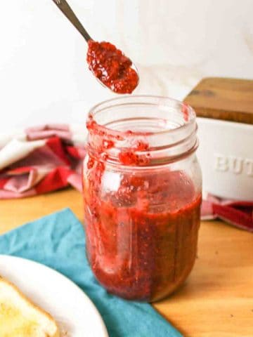 a spoon holding up a bit of strawberry jam above a jar