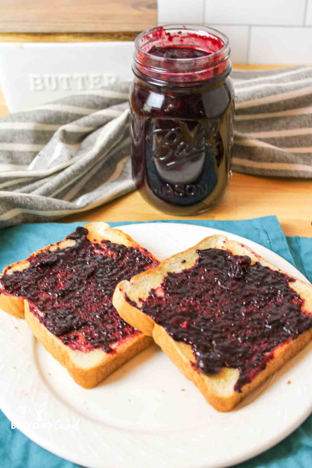 two slices of toast topped with sugar free blueberry jam and a jar full of jam in the background