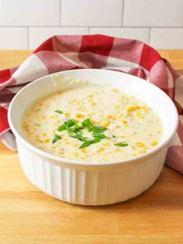 a round white casserole dishfilled with creamed corn and topped with sliced green onions