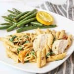 roasted garlic and tomato pasta with chicken and a pile of green beans and lemon slice in back.