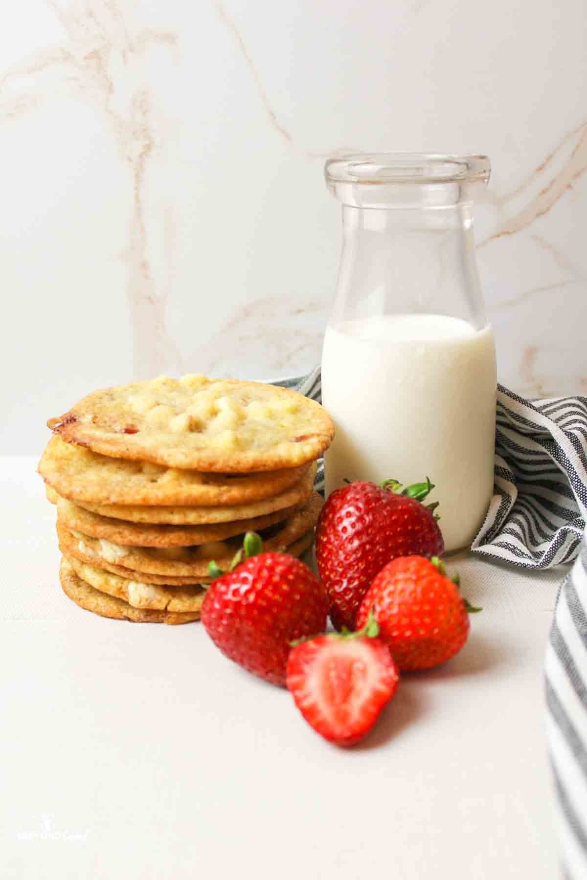a bottle of milk next to fresh strawberries and cookies stacked.