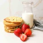 a close up of a stack of strawberries and cream cookies with fresh strawberries and a bottle of milk to the side