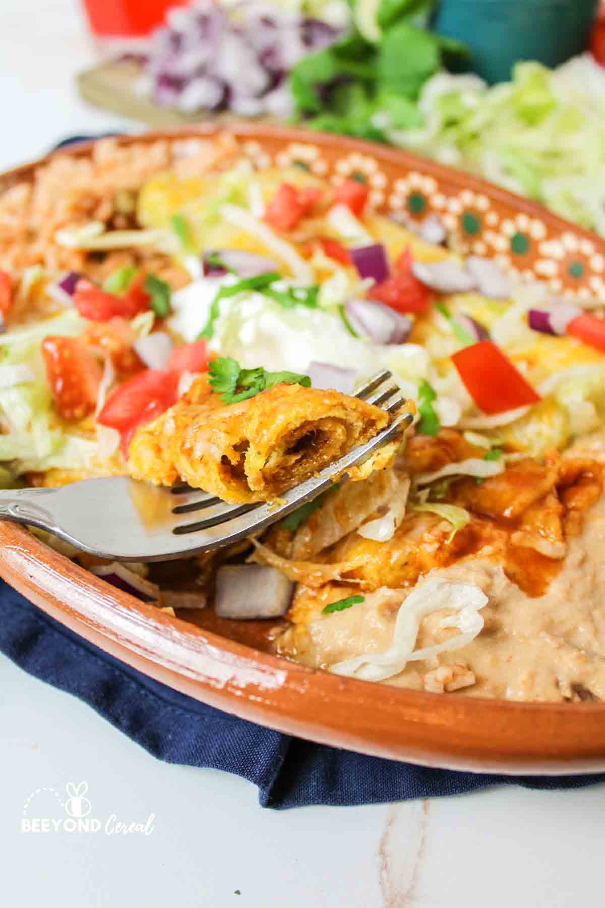 beef enchilada with a bite on a fork resting on the plate.