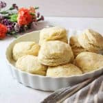 an uplcose view of a dish full of baking powder biscuit with fresh flowers in background