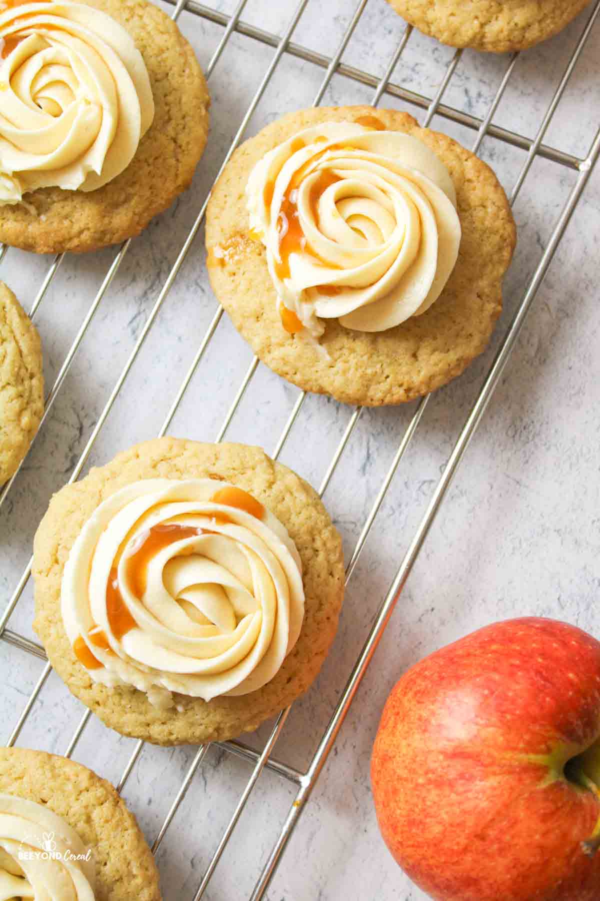 aerial view of caramel buttercream topped cookies on a wire rack with a red apple to the side