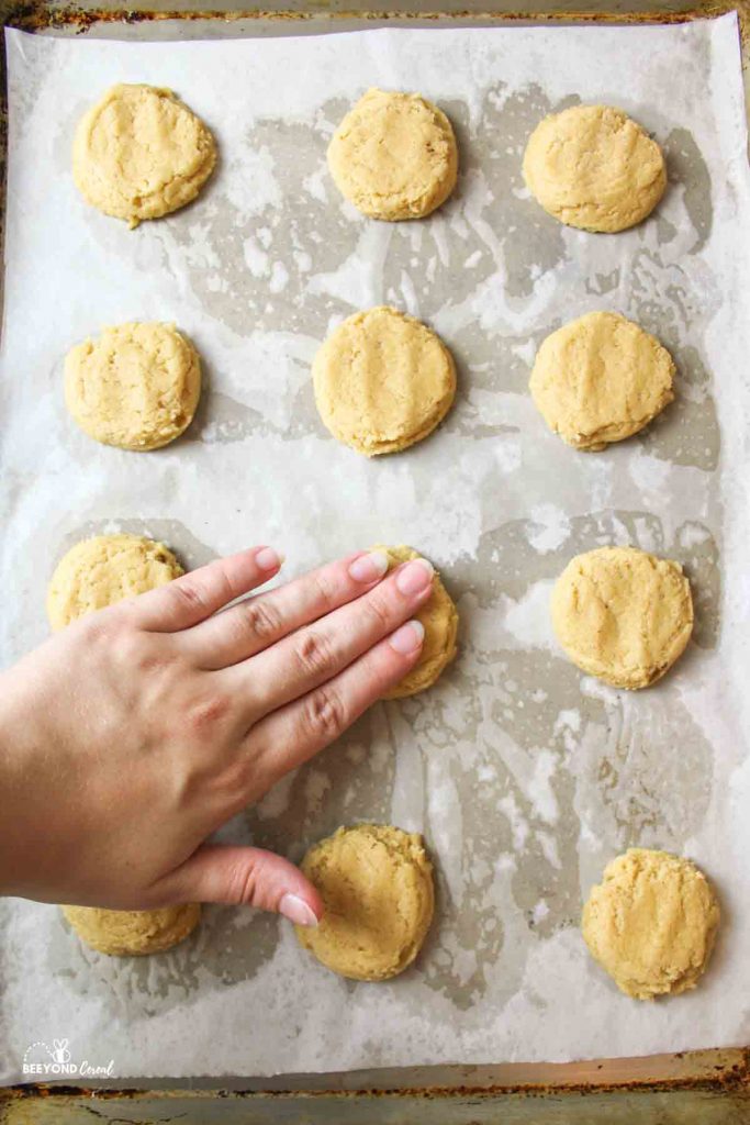 a hand lightly pressing down on cookie dough balls to make them flatter