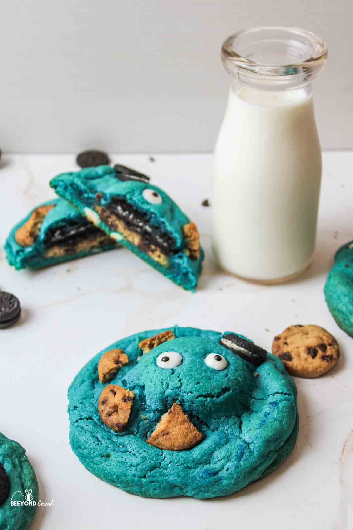 a blue cookie with eyes and topped with cookies with a broken cookie in background to reveal cookies inside