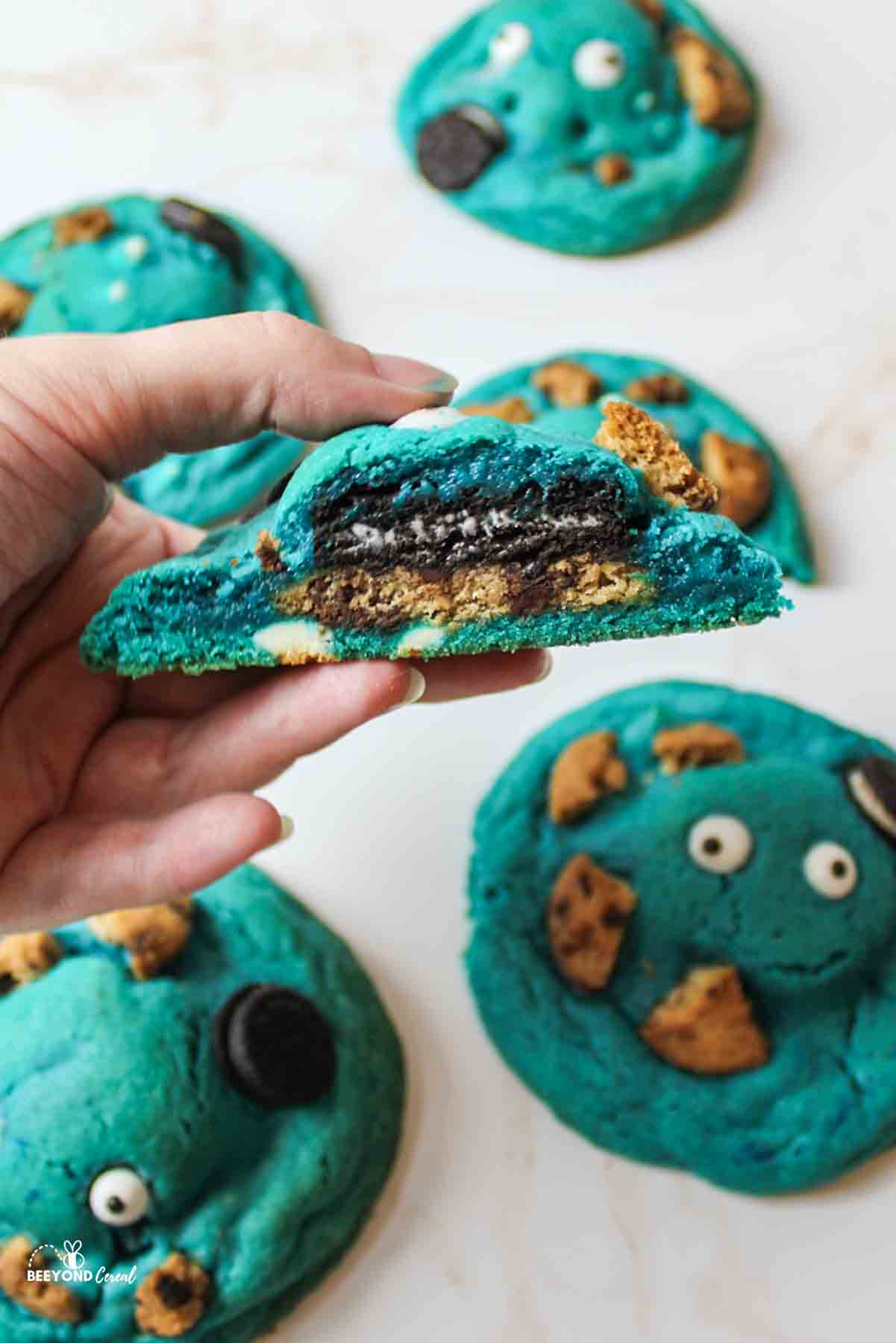 a hand holding up half of a cookie monster cookie above other scattered cookies