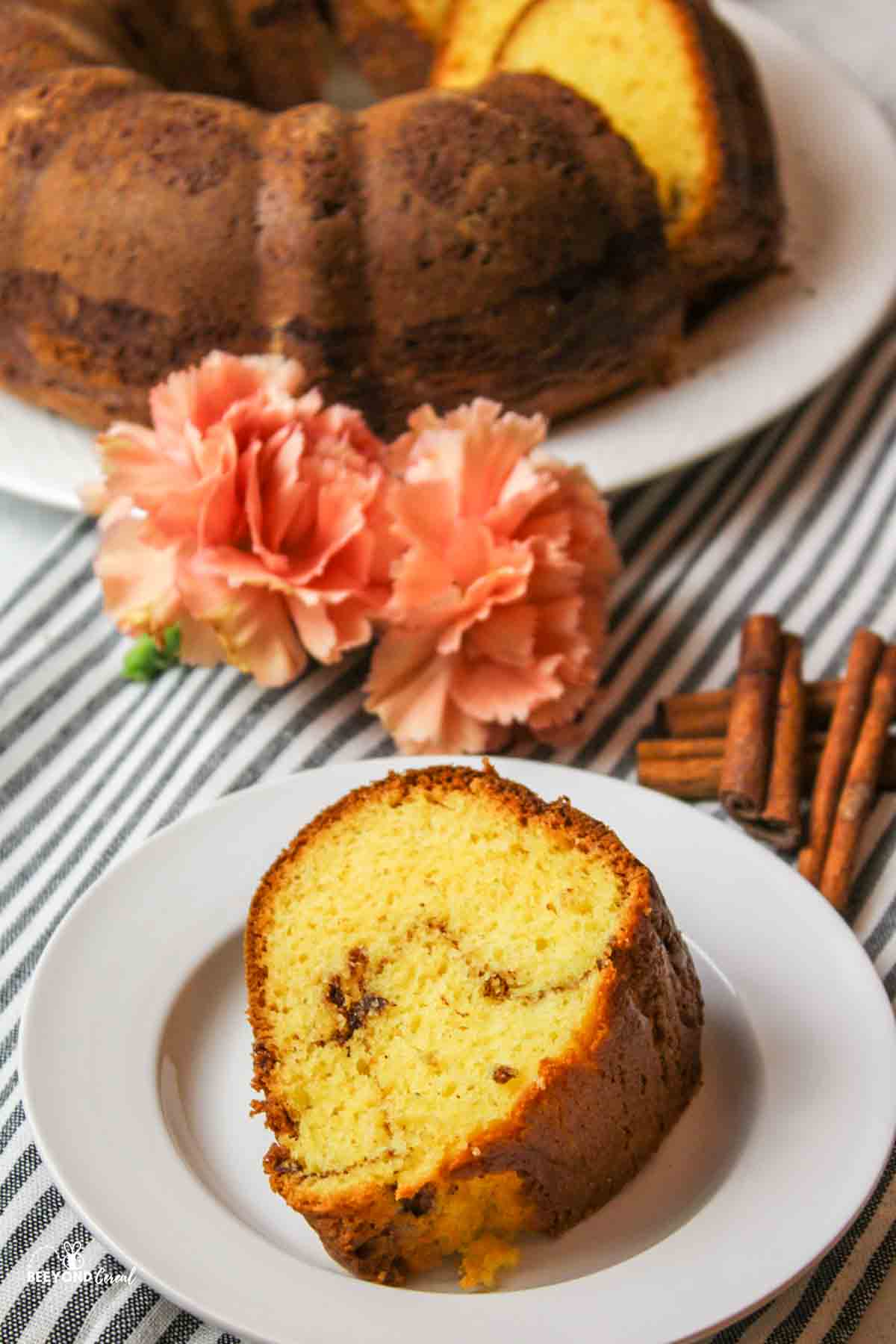 a slice of coffee cake on a plate with flowers and cinnamon sticks to the side.