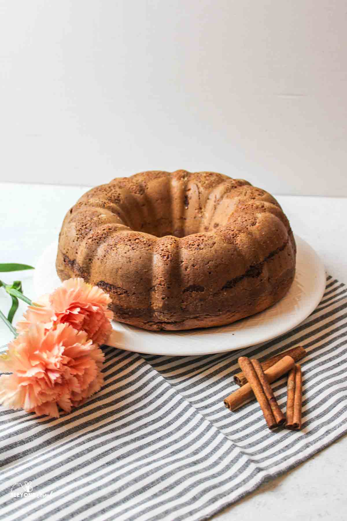 bundt coffee cake next to fresh pink flowers and a pile of cinnamon sticks