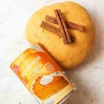 a ball of pumpkin playdough with two cinnamon sticks on top and a can of pumpkin puree to the side.