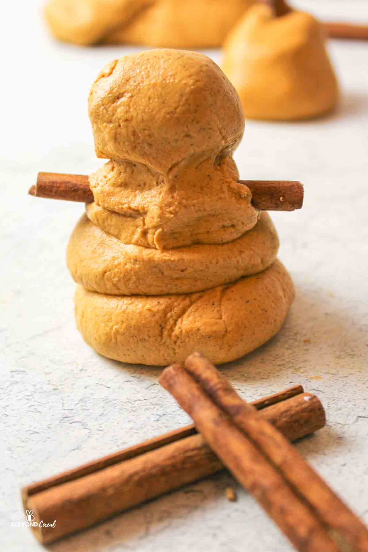 a small snowman shape made from pumpkin playdough with cinnamon stick arms and cinnamon sticks in front