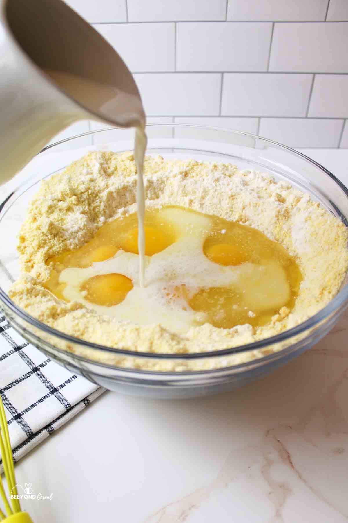 pouring milk into a bowl of other cornbread ingredients.