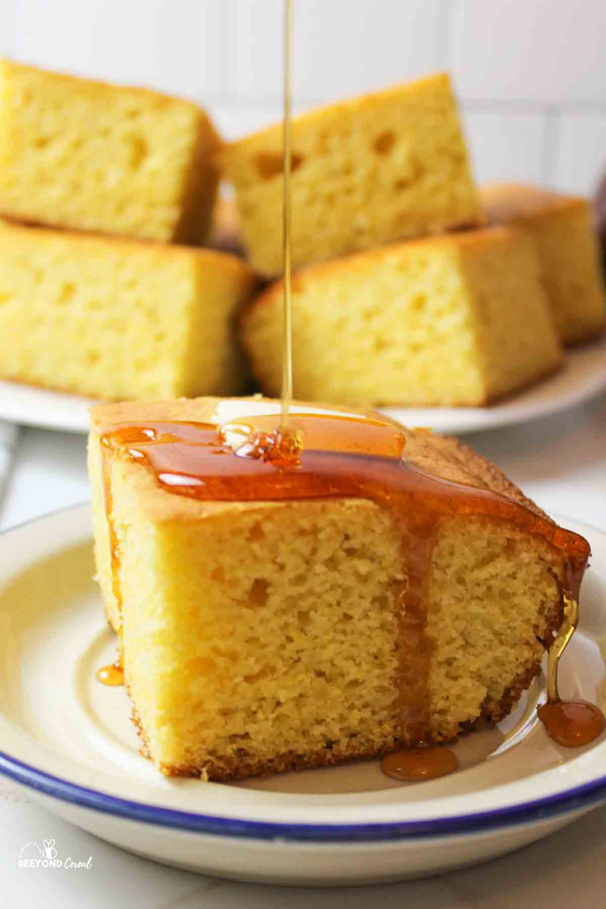 honey being drizzled on top of a butter topped slice of cornbread on a plate.