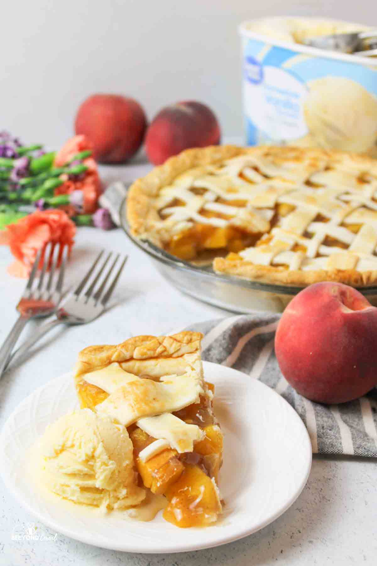 a sliced peach pie with ice cream in front and more pie and fresh peaches in background