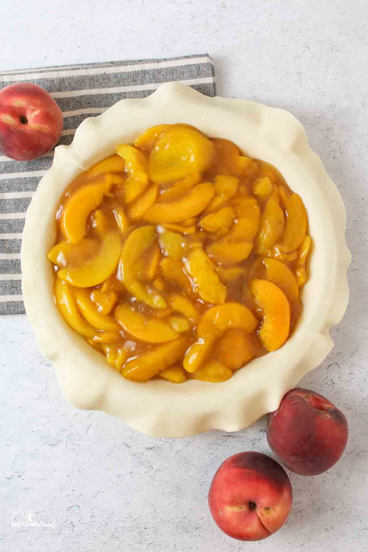 an aerial view of a peach pie without a top and fresh peaches to the sides