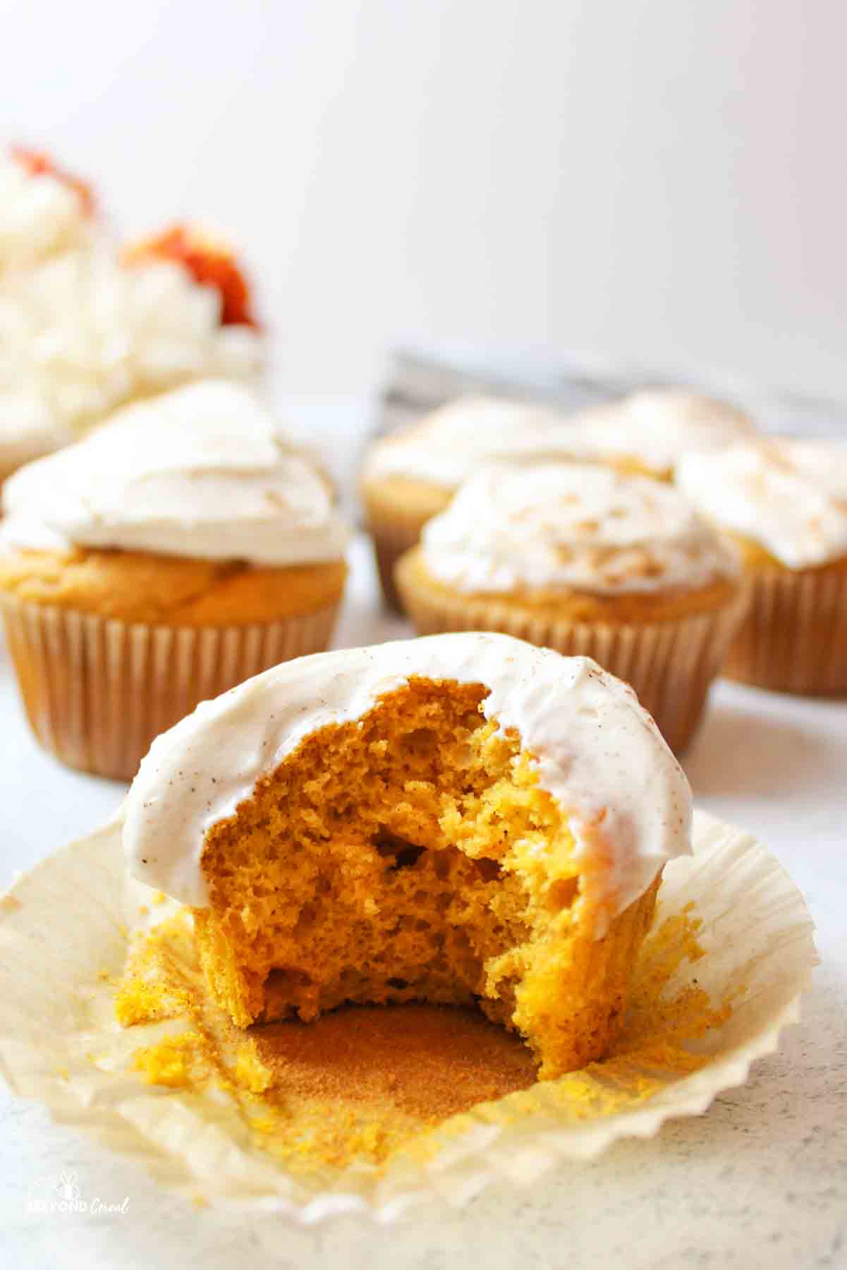 a cream cheese frosted pumpkin cupcake with a bite taken out of it