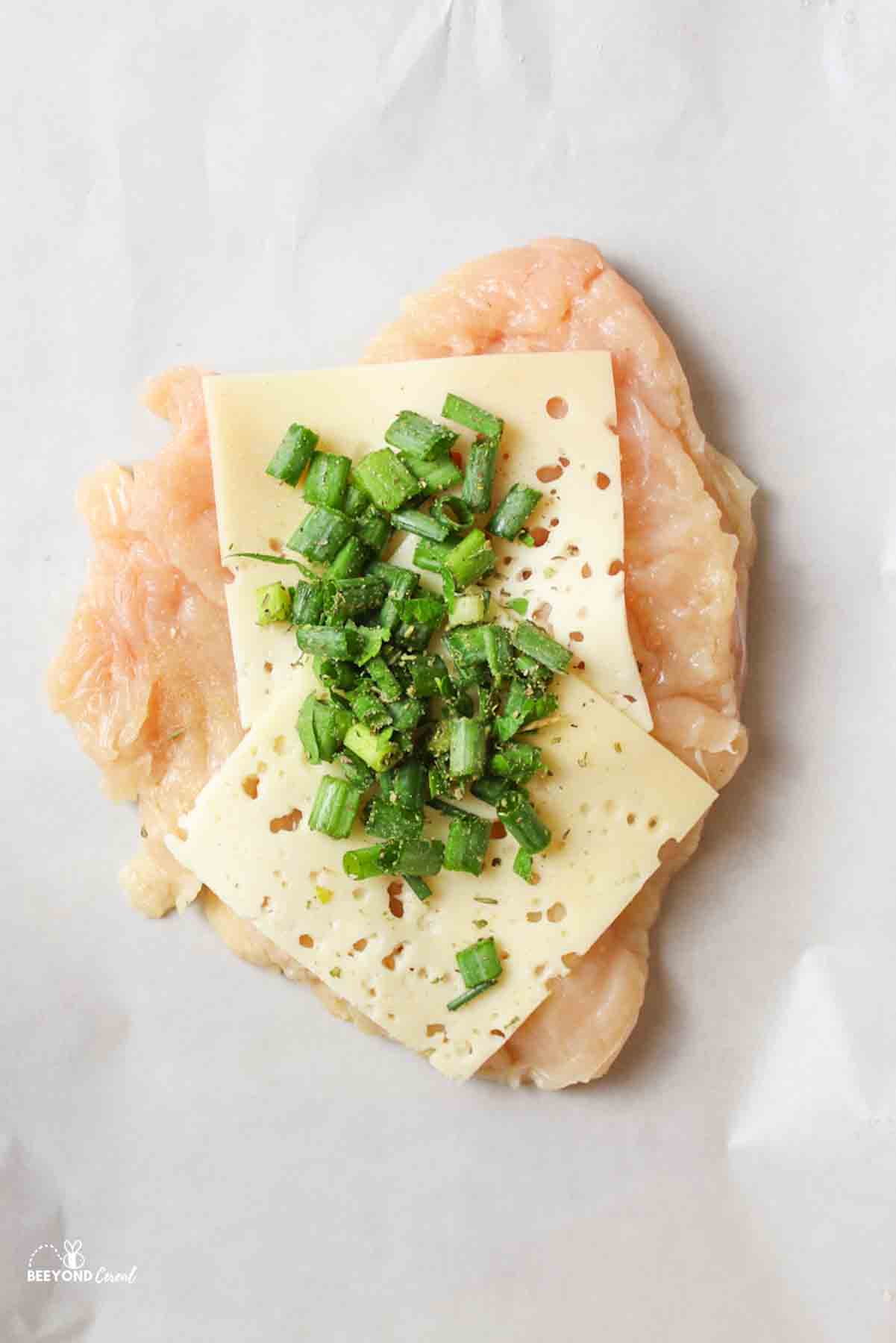 an open chicken breast with sliced swiss cheese and a green onion filling on top.