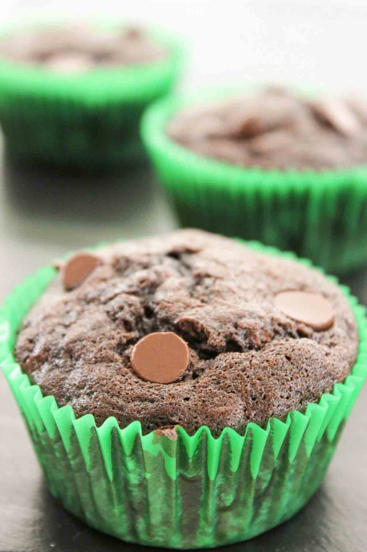 an upclose view of a chocolate zucchini muffin with chocoalte chips in a green muffin liner