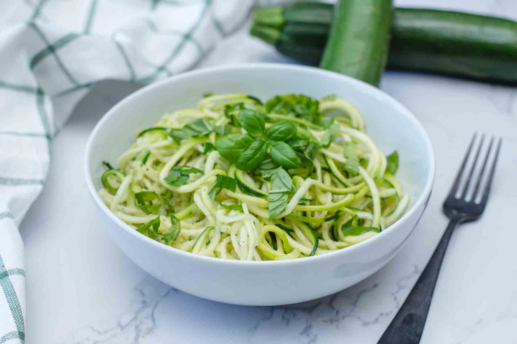 a photo of a bowl of zucchini noodles next to a fork