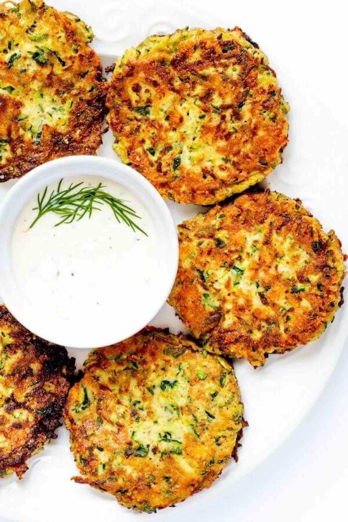 a photo of zucchini fritters next to a small bowl of dip