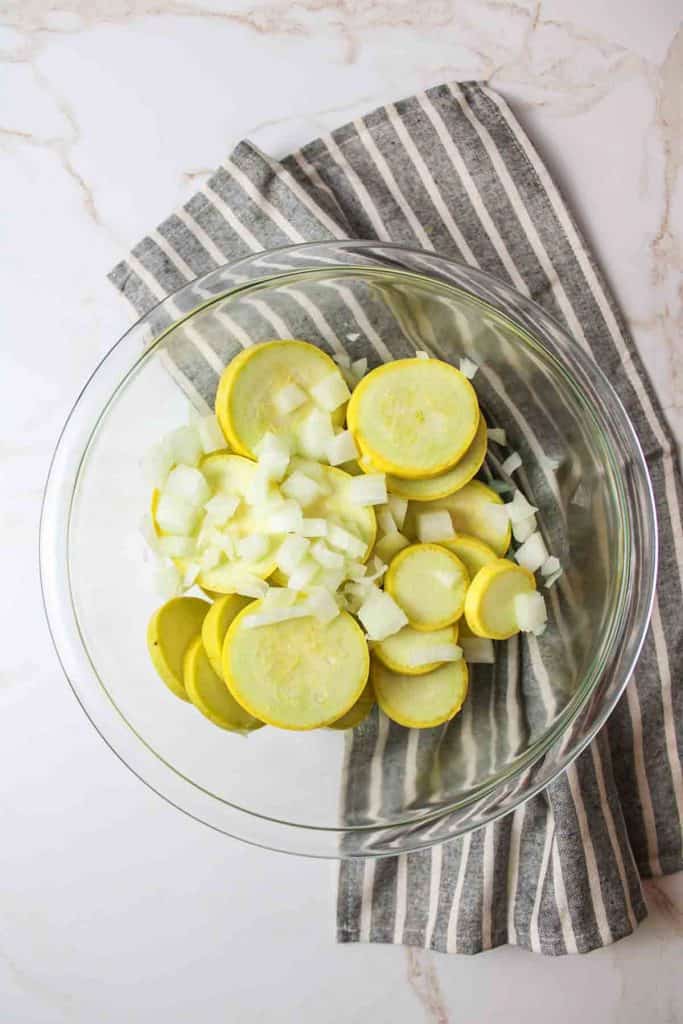 a glass bowl full of diced onion and sliced yellow squash