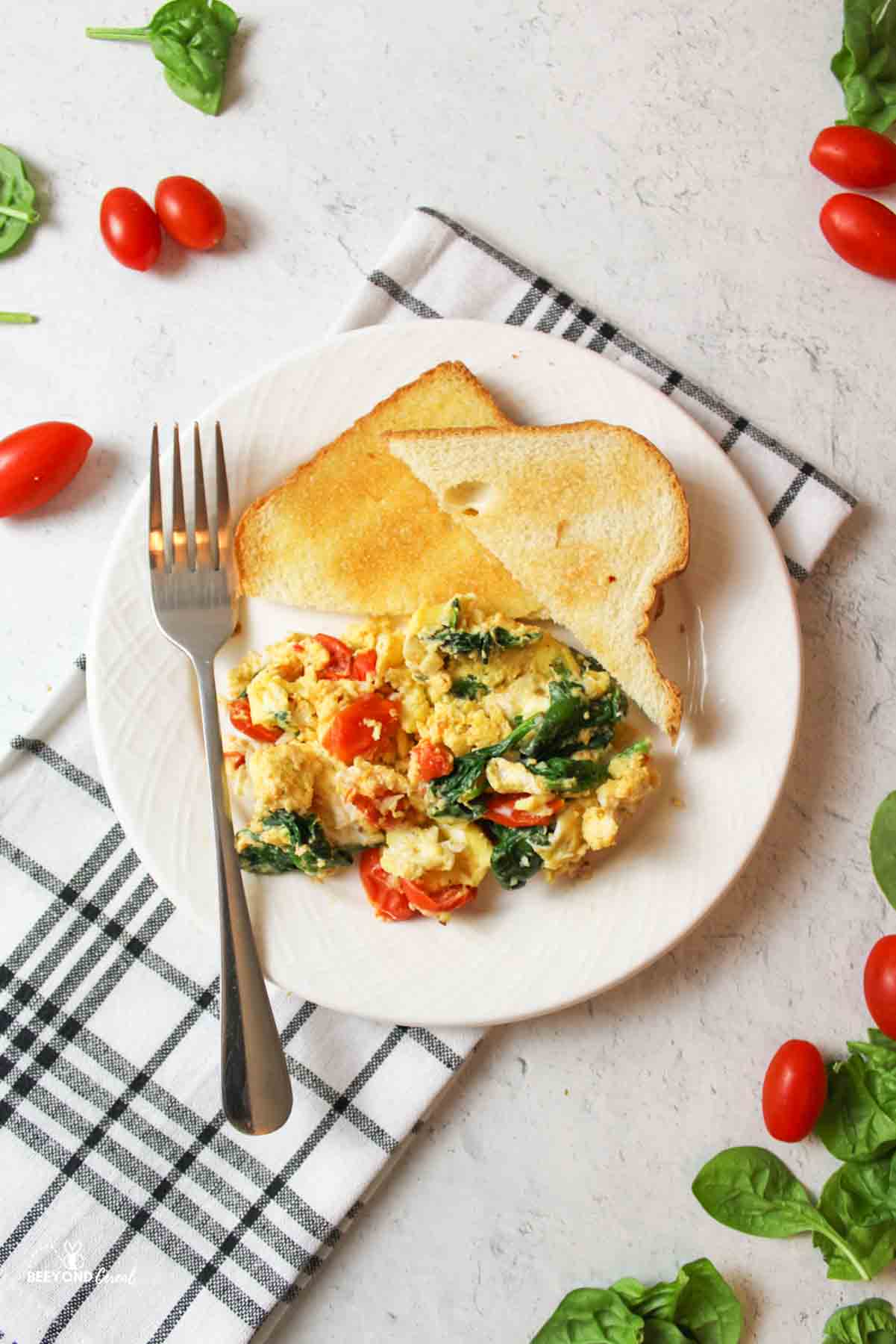 aerial view of a plate filled with Scrambled Eggs with Spinach and Tomatoes, two pieces of toast and a fork