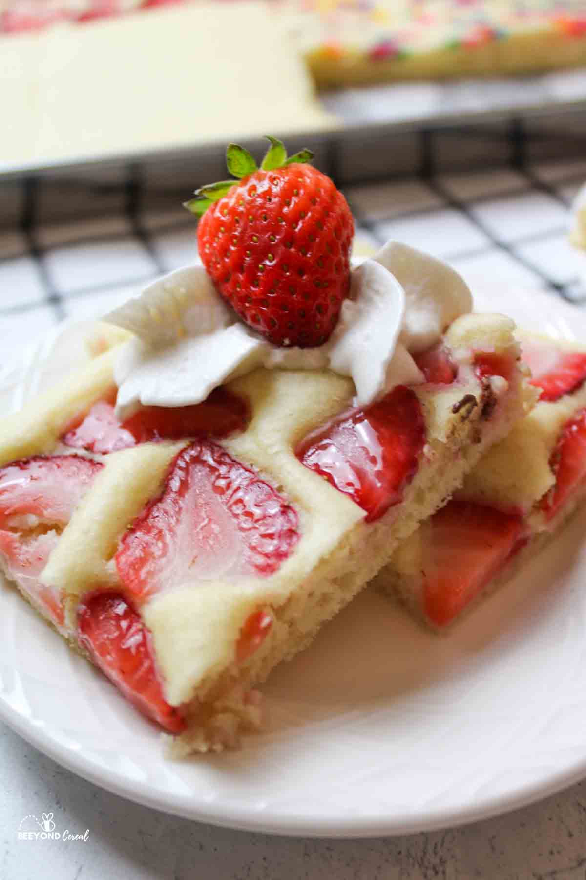 strawberry sheet pan pancake on a plate with whipped cream and a fresh strawberry on top