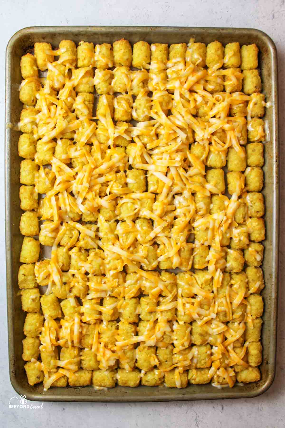 cheese on top of tater tots on baking sheet.