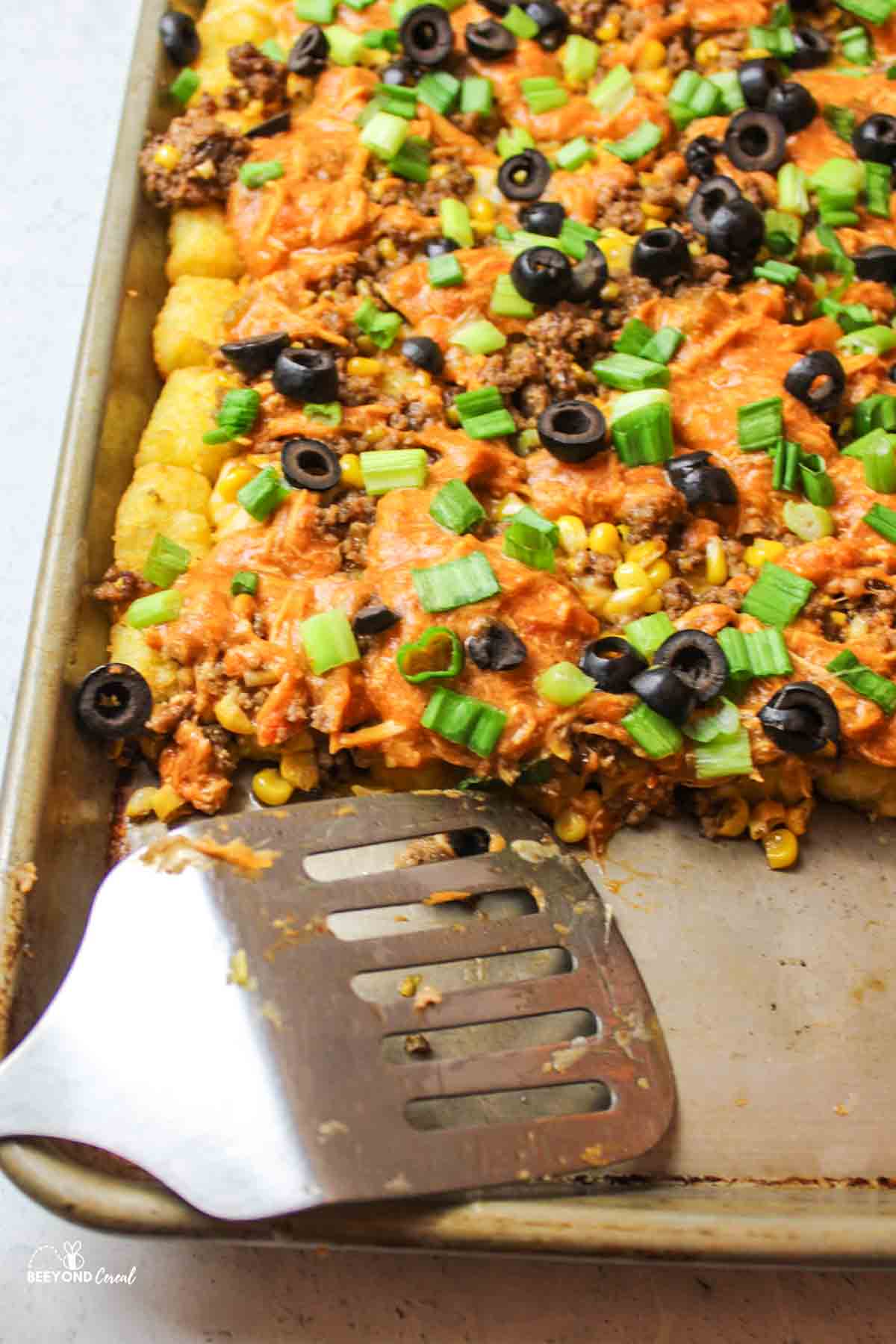 a metal spatula on a baking sheet of totchos with some servings missing