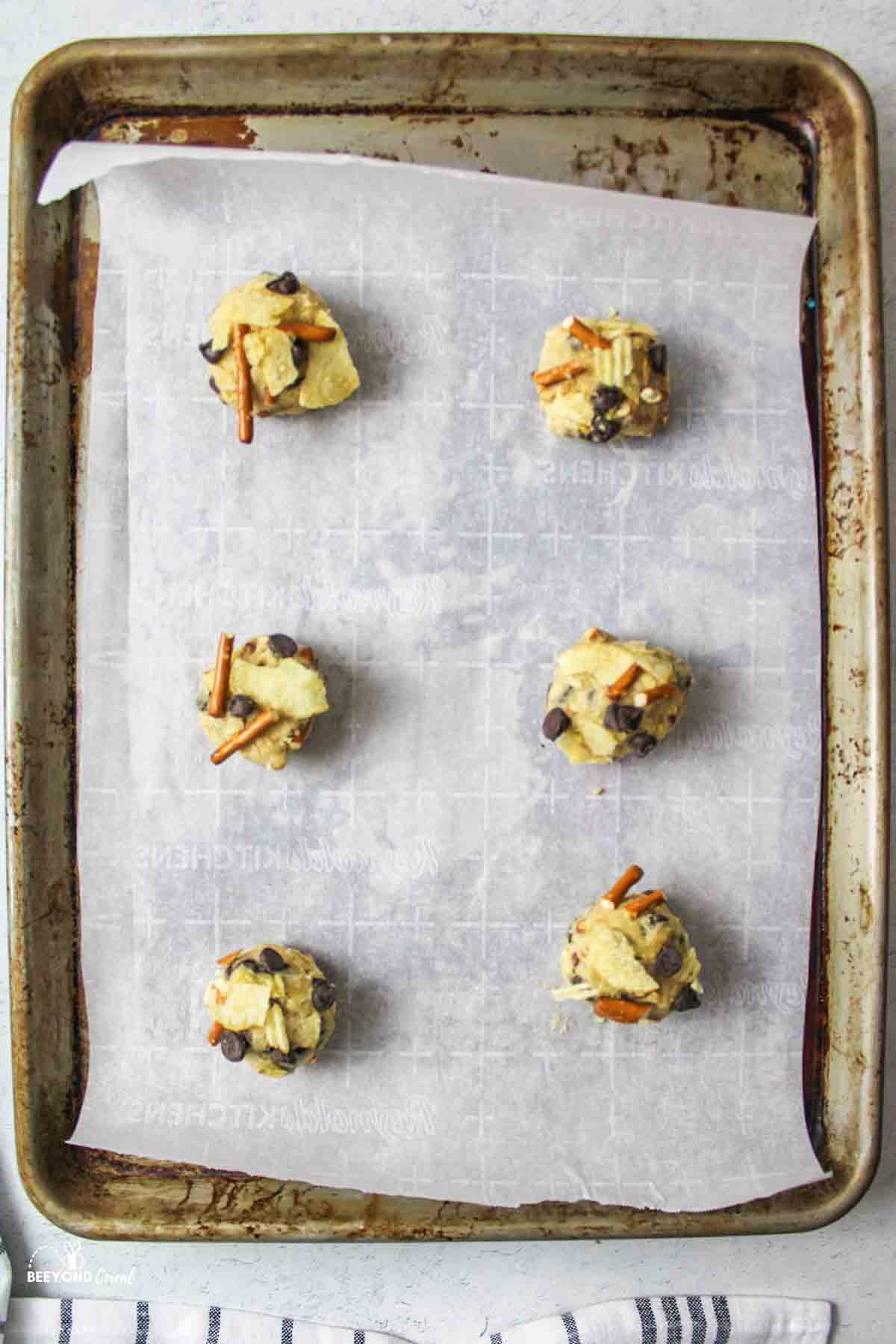parchment paper lined baking sheet with several choc chip pretzel chip cookie dough balls on top.