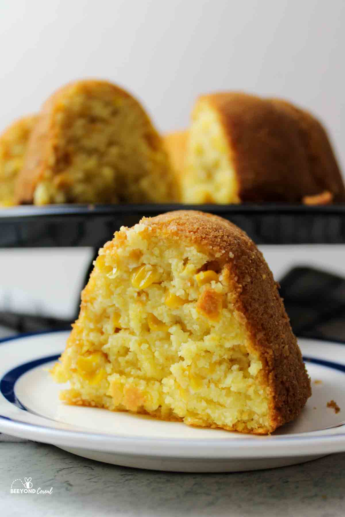 a slice of cornbread bundt cake with the rest of the cake in the background.