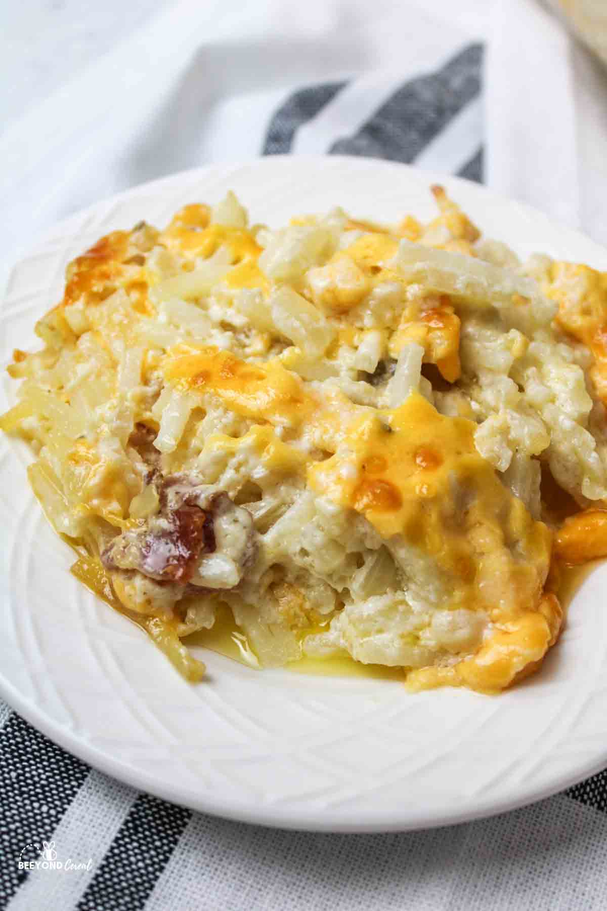 a close up of cheesy hashbrown casserole on a white plate