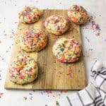 giant rainbow sprinkle cookies arranged on a wooden cutting board covered in scattered sprinkles