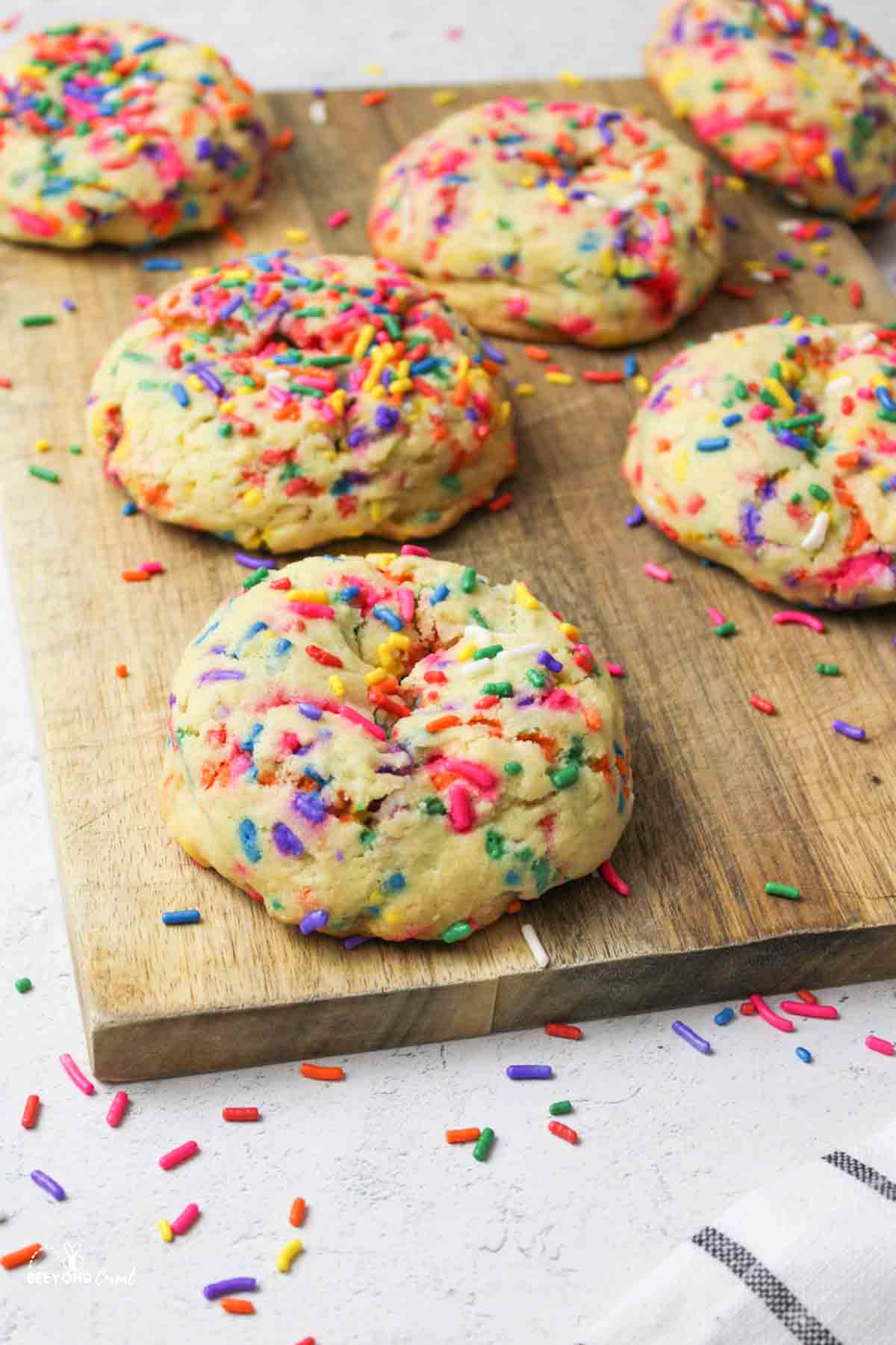 sprinkle cookies on a wooden cutting board with scattered sprinkles