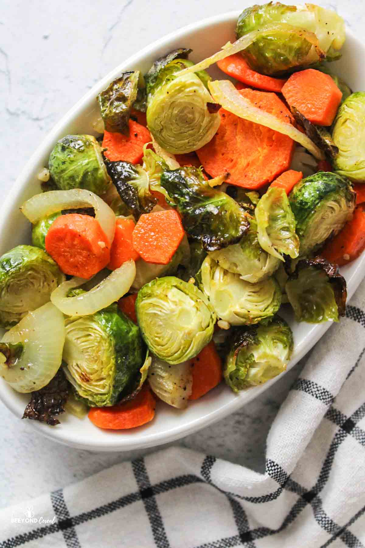 an oval bowl filled with roasted brussel sprouts and carrots.