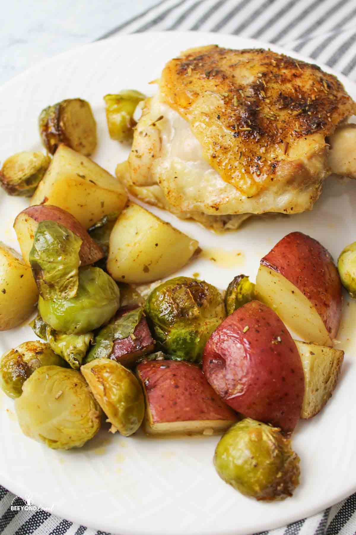 chicken thigh, brussel sprouts, and red potatoes on a white dinner plate.
