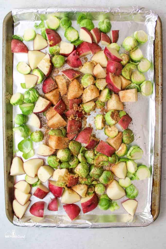 seasoning and garlic over brussel sprouts and red potatoes on a foil lined baking sheet