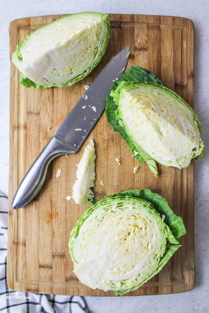 cabbage cut in half and quartered with large knife on wooden cutting board
