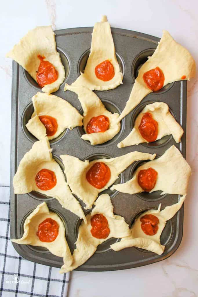 crescent rolls in muffin cups with a dollop of pizza sauce in each center