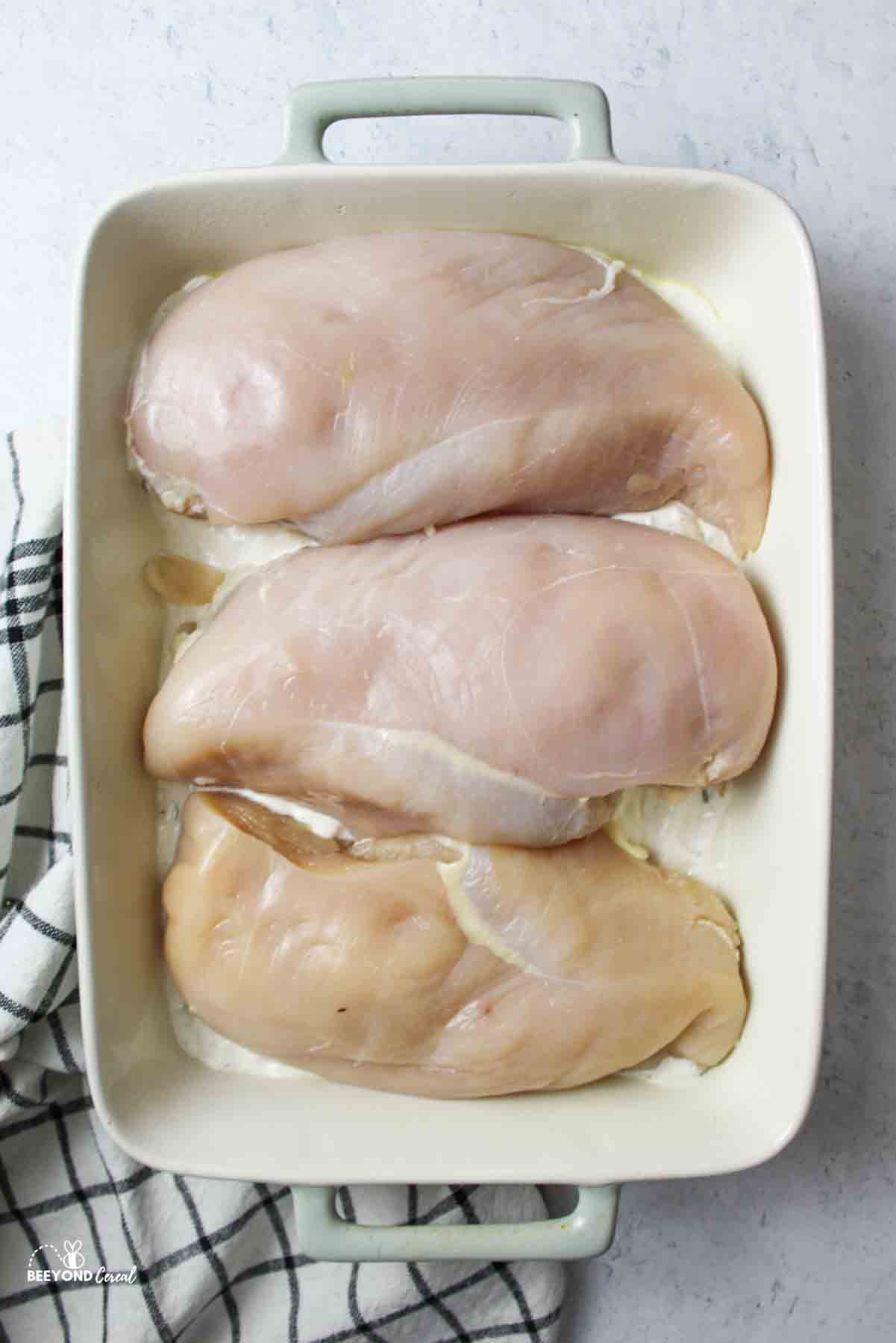 three raw chicken breasts in a baking dish
