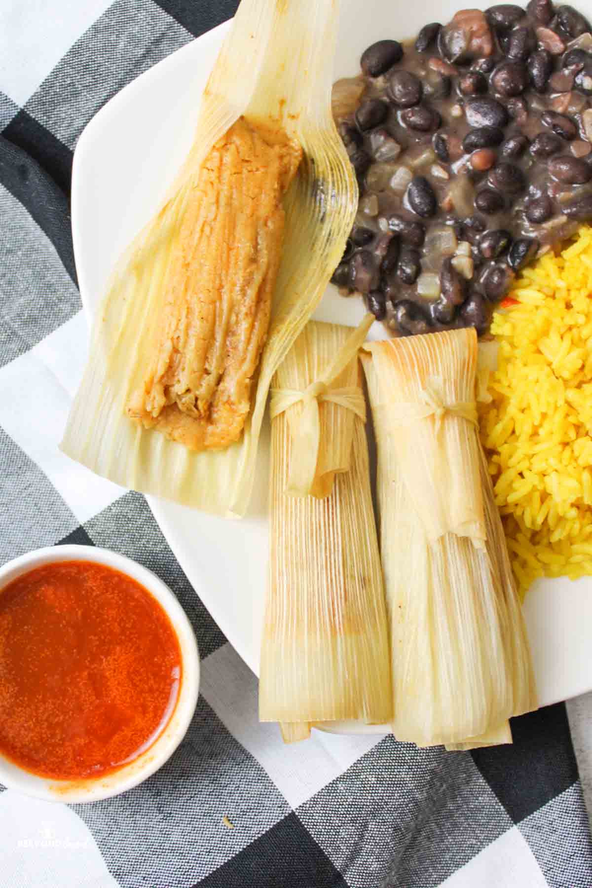 three turkey tamales on a plate with side dishes one tamale is opened to revel the doughy inside