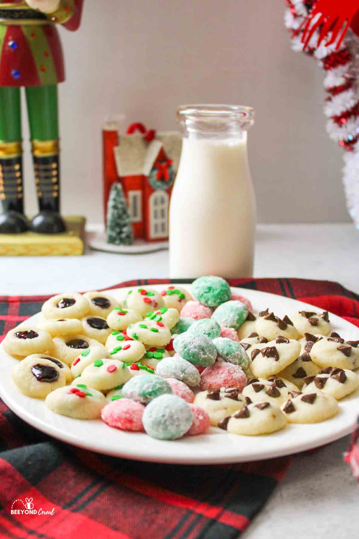 a plate topped with tiny cookies and a glass bottle of milk in the background